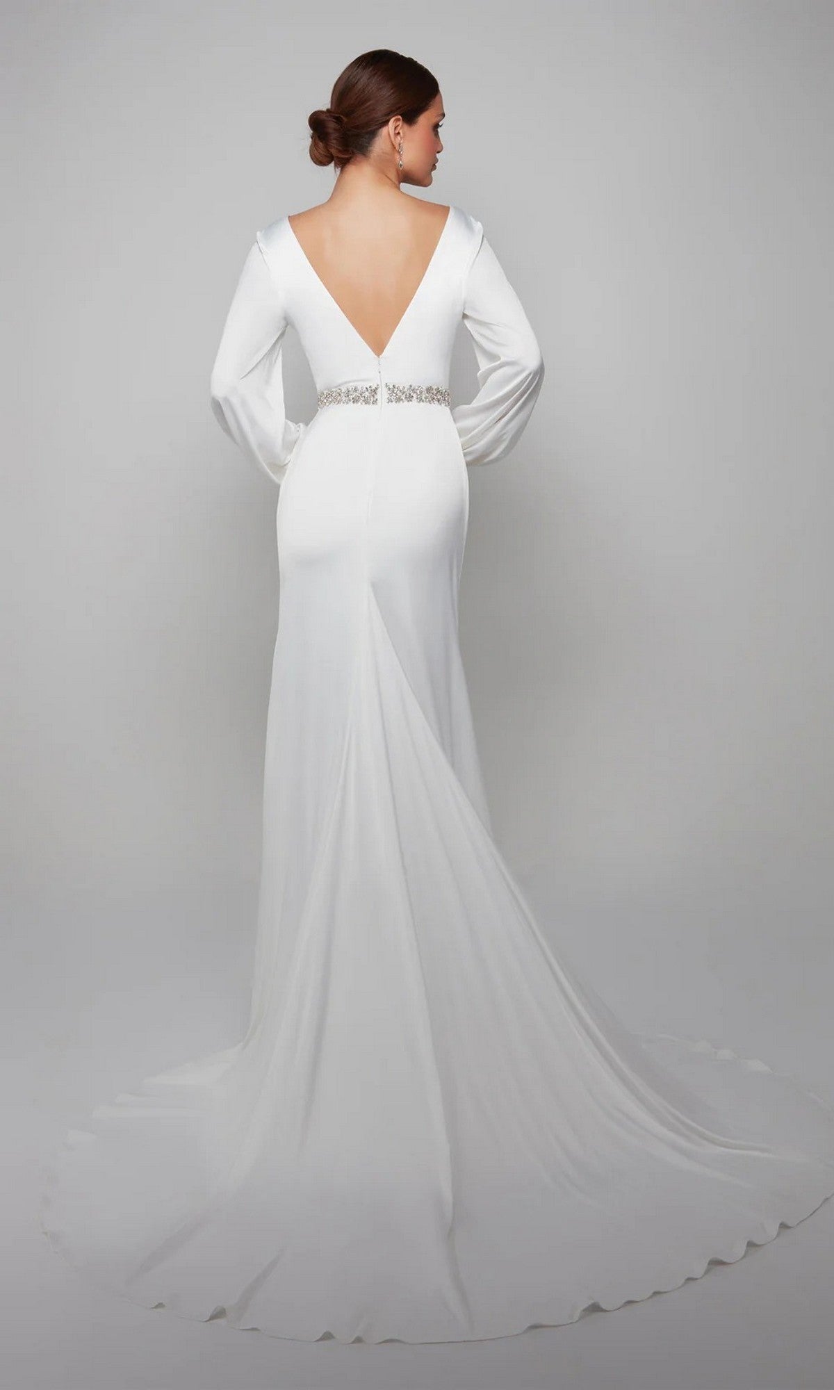 A woman poses against a plain light background wearing the Alyce 7070 long formal dress—a satin gown with a deep V-back, fitted waist with jeweled belt, and flowing train—ideal for evening events.